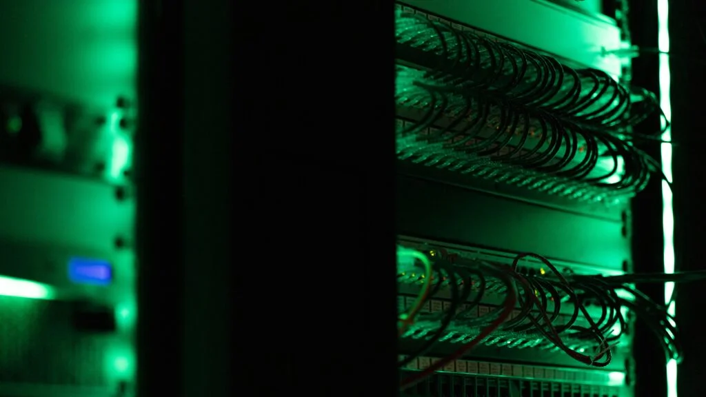 Server rack in green light with coiled cables connected to a port panel and a server unit with a blue indicator light.